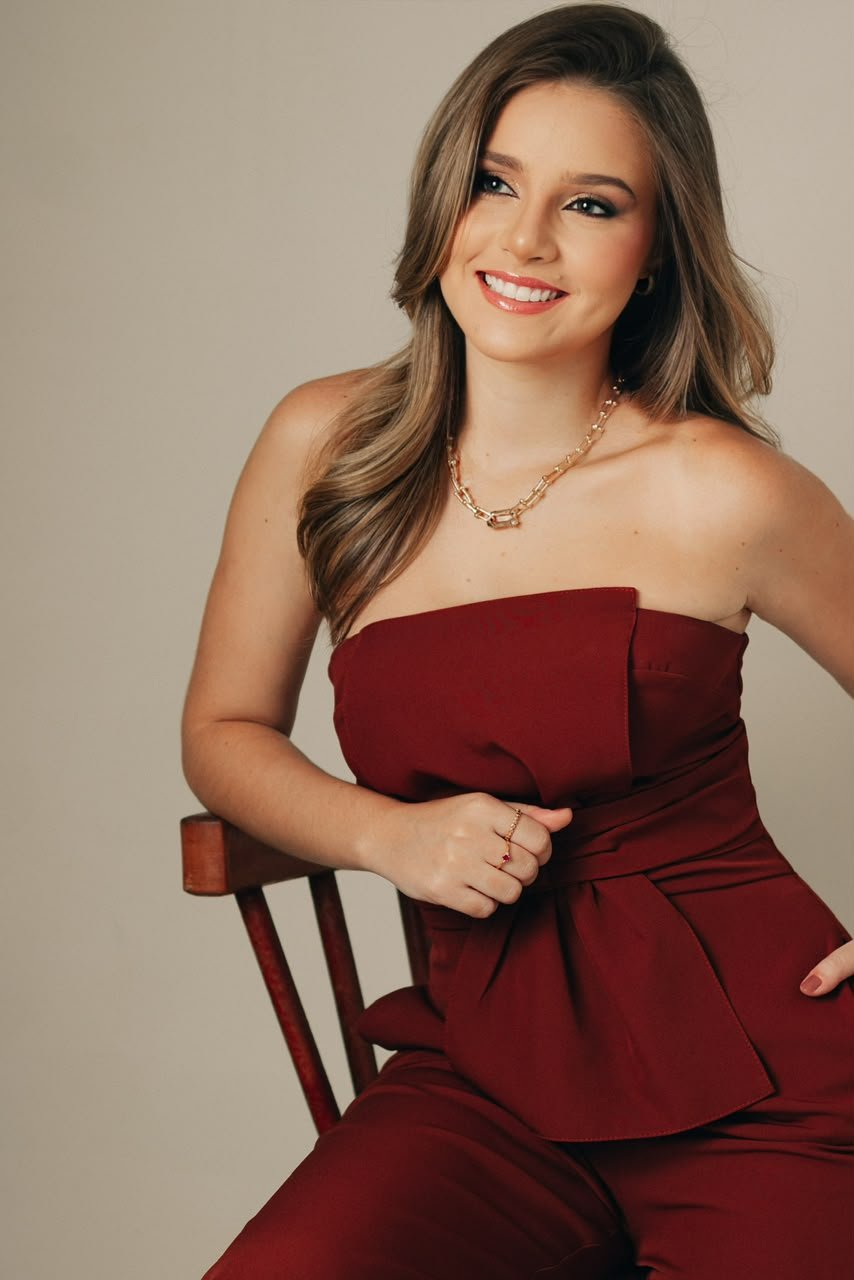 Dra. Gabriela Nasiasene sorrindo, sentada numa cadeira de madeira